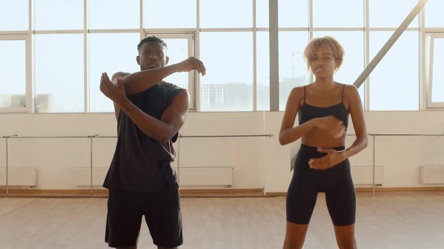 Young Black Couple man and woman stretch their arms side by side in a sunlit dance studio, preparing for a joint workout or dance rehearsal and emphasizing fitness, teamwork, and healthy lifestyles