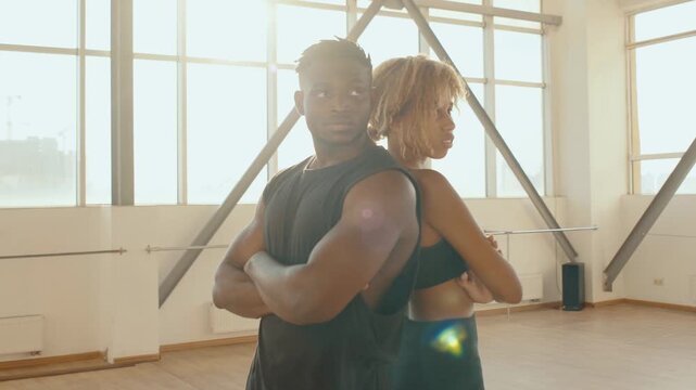 African Fitness Couple Back-to-Back in Bright Studio Gym Portrait Showing Confidence and Strength, and woman and man trainers stand in the fitness room, in sunlight fitness and healthy lifestyle 4K