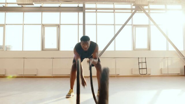 Focused Young Man Doing Battle Rope Workout in Bright Gym Training for Strength and Endurance