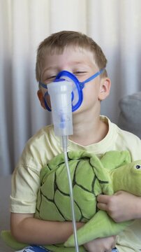 Child uses nebulizer inhaler mask with stuffed frog toy for comfort during home breathing treatment. Pediatric anxiety relief and gentle respiratory illness therapy concept. 