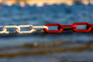 Red and White Chain Link by the Sea Symbolizing Connection, Contrast, and Nautical Boundary © Noel