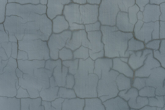A gray textured concrete wall covered with a network of fine cracks. A close-up shot of a weathered cement surface with abstract craquelure patterns.