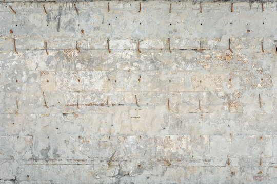 A distressed white block wall structure with rows of bent metal loops. An industrial damaged plaster surface texture.