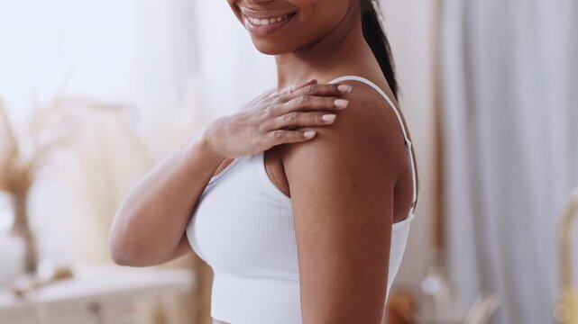 Smiling Black Woman With Healthy Skin Showing Off Her Shoulders In Bright Home Setting. Happy Female Looking Confident And Proud While Taking Care Of Her Skin. Skincare Concept.