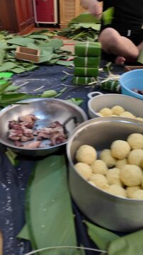 Vietnamese family making chung cake together for Tet holiday at home, Vietnam lunar new year, traditional food with ingredient sticky rice, mung beans, meat wrapping by green dong leaves
