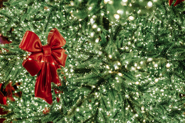 Obraz premium Red bright Christmas bow hanging on a decorated Christmas tree, festive holiday seasonal golden green background