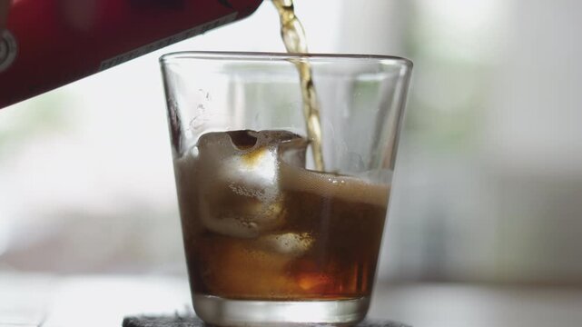 Close up of pouring dark carbonated soda into a glass filled with ice cubes. Refreshing cold beverage with fizz and bubbles. Summer thirst quenching and cooling drink concept.