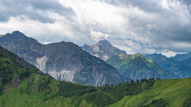 mountain range from little valley of Walser with green meadows and steep rocky slope in the alps of Bregenzerwald, with rocky mountains and steep, stony slopes on a rainy day with clouds.
