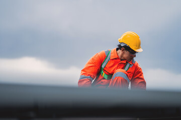 Obraz premium Asian Male Engineer in Orange Safety Suit Cleaning Solar Panel Surface on Rooftop. Solar Panel Maintenance and Cleaning in Renewable Energy Operations.