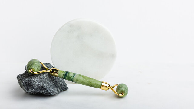 Green jade roller massager for face on white marble.