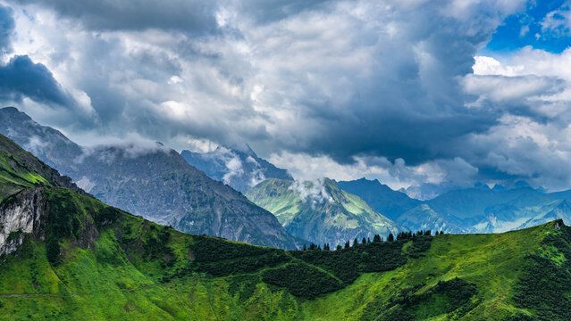 mountain range from little valley of Walser with green meadows and steep rocky slope in the alps of Bregenzerwald, with rocky mountains and steep, stony slopes on a rainy day with clouds.
