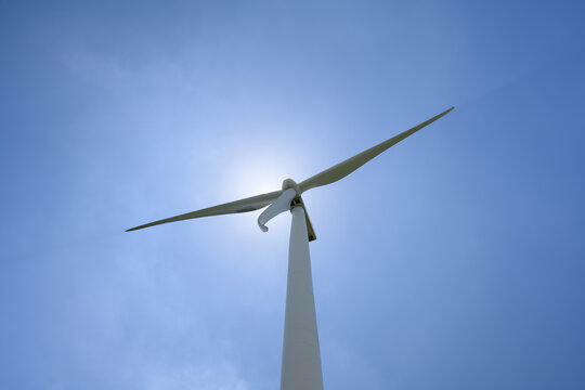Sunburst Behind Wind Turbine Blades Against a Clear Blue Sky