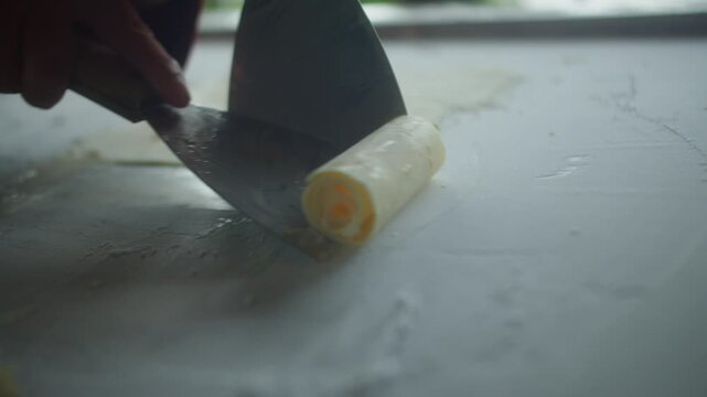 Close up of chef spreading mango ice cream on a frozen pan and carefully rolling it into neat ice cream rolls. Fresh homemade frozen dessert prepared by hand.