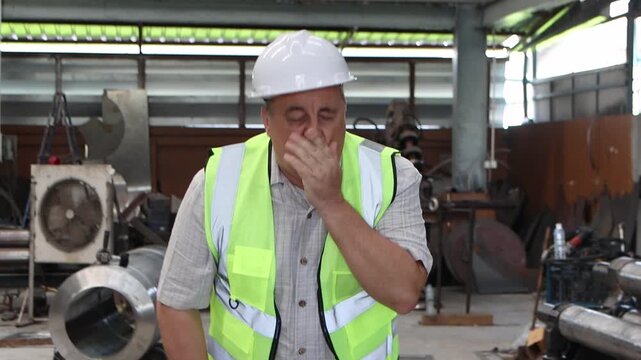 Elderly engineer with safety vest and helmet feels dizzy, fainting while walks around to inspect workplace factory, then Asian female worker comes to help and support senior foreman who feels unwell.