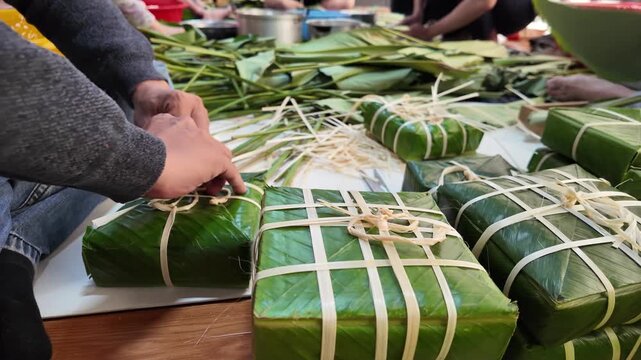 Close up hand tying the pair of chung cakes with bamboo string, Vietnamese family making traditional food together for Tet holiday at home, Vietnam lunar new year