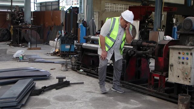 Industrial elderly engineer worker with safety vest and white helmet feels dizzy and fainting while walks around to inspect workplace at factory. Senior foreman feeling unwell and having a headache.