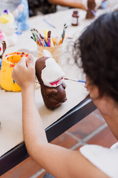 hand of artist kid girl with brush painting ceramic figure at terrace in latin America