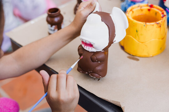 hand of artist kid girl with brush painting ceramic figure at terrace in latin America
