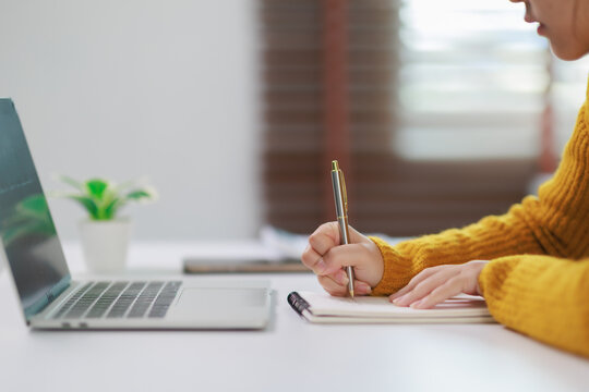Woman working and studying from home, watching online lessons on her laptop, writing notes in a notebook, learning and educating herself for a new career