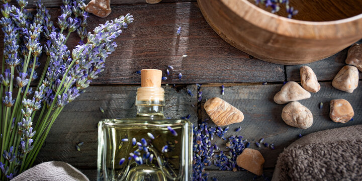 Natural aromatic experience. Lavender essential oil surrounded by fresh lavender blossoms on a rustic wooden surface. Close-up, top-down view.