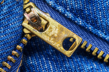 Close-up of a golden metal zipper pull and teeth on blue denim fabric texture © dimas830