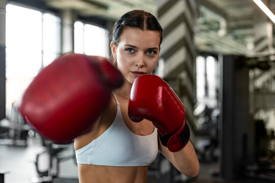 Young woman boxer athletic wearing gloves strikes punching bag during training preparation for battle.
