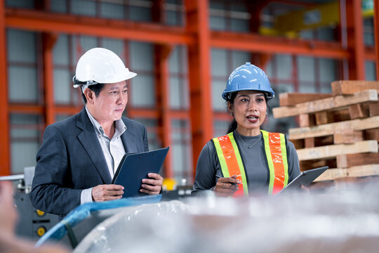 professional engineer,worker,technician use clipboard discuss work, walk in steel metal manufacture factory plant industry. Black African American man and woman wear hard hat check quality machine.