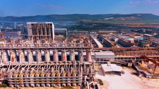 Industrial processing installation with row of tall vertical columns. Aerial close up of chemical refinery plant cylinders, intricate pipes, white dust material yard.