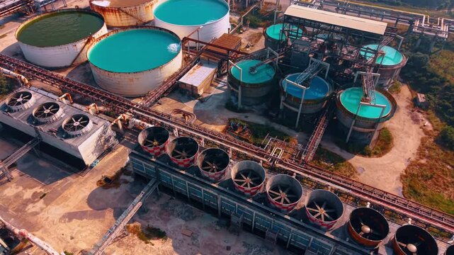 Circular chemical treatment reservoirs with turquoise liquid at facility. Drone view of open water clarification basins, industrial cooling systems, green landscape border.