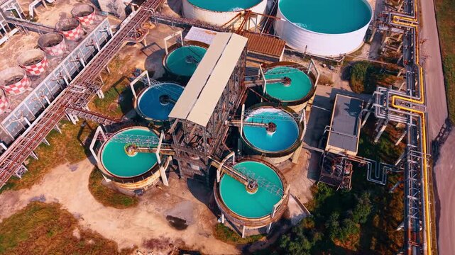 Aerial view of industrial wastewater treatment tanks with turquoise water.. Circular clarification pools with bright blue water are captured from above at a chemical plant facility.