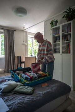 Woman preparing for holiday trip, placing and checking order of accessories and cosmetic bag in suitcase, relaxed female getting ready for vacation and organizing personal clothes in travel case.