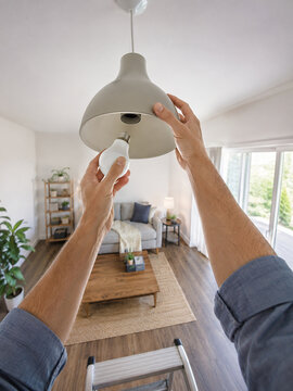 Hands replacing a ceiling light bulb indoors, illustrating simple household electrical maintenance, lighting upkeep, and everyday do-it-yourself home care.