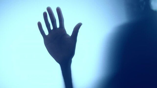 Man slowly moving hand along matte glass in blue light. Mental health and anonymity concept