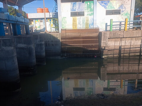 Sluice gate at river mouth during low tide with dramatic sunset sky, flood control infrastructure