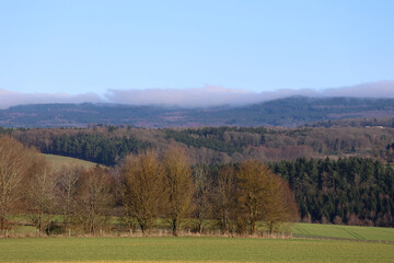 Fototapeta premium Wide landscape view of the forested Soonwald ridge with farmland and low clouds near Schönborn in Rhineland-Palatinate, Germany.