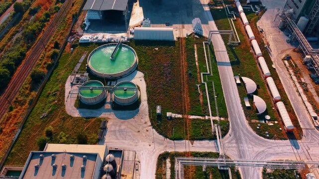 Wastewater treatment facility with circular green pools from above. A top down drone shot captures three round tanks containing bright liquid next to cargo train cars.