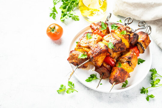 Grilled meat on skewers on light stone table.