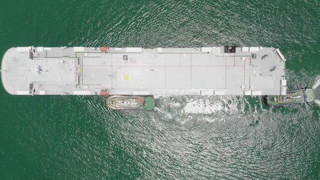 Large cargo ship receives careful assistance from agile tugboats during controlled docking operations within dark ocean waters at industrial port location featuring Oil tanker