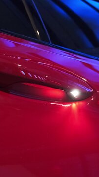 Close-up of red high-performance sports sedan door handle recess with soft spotlight reflection on glossy metallic bodywork. Premium luxury performance car exterior detail for automotive editorial con