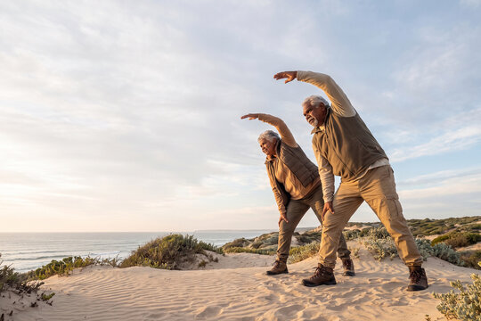 Active Senior Couple Practicing Beach Stretching Exercises for Healthy Aging Fitness
