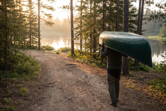 Person Carrying Canoe Along Forest Trail Toward Peaceful Lake Adventure