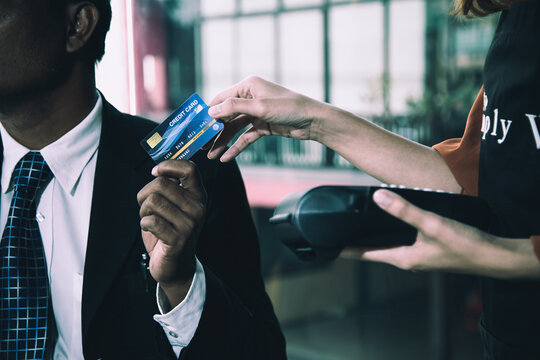 Businessman handing a credit card to cashier holding a payment terminal, showing retail purchase, finance, transaction, banking, commerce, checkout, and cashless payment
