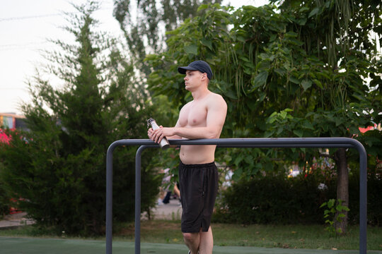 A man exercises at a fitness park in the evening while holding a water bottle and looking relaxed
