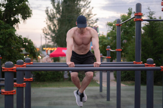 A man trains on fitness bars in a park as the sun sets, focusing on his workout routine