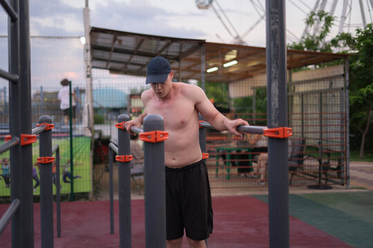 A man exercises on fitness bars in a community park during the evening hours near a playground