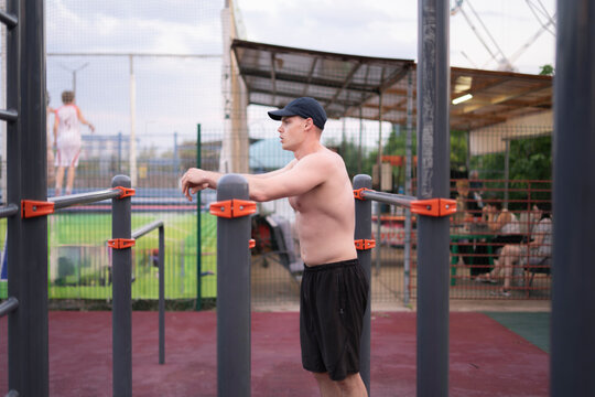 A man performs a workout on bars in an outdoor gym with other people sitting in the background during the afternoon