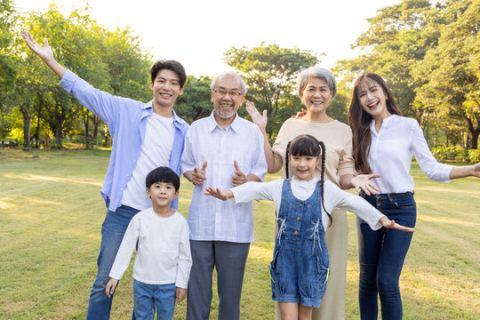Happy multi-generational Asian family smiling together in a sunny green park. Grandparents, parents, and kids enjoying outdoor quality time, promoting family bonds, health, and togetherness