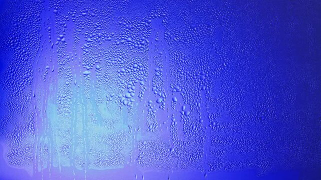 Closeup video portrait of anonymous young black woman with afro hairstyle behind wet matte glass in blue light. She is turning face and going away. 