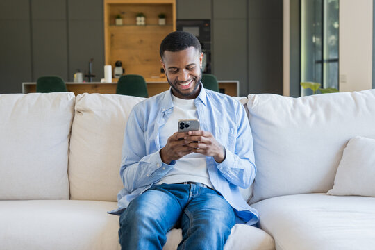 African american man relaxing on a comfortable couch at home, enjoying wireless technology and connecting with friends or browsing online content on his smartphone