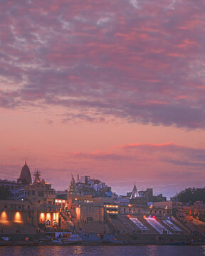 Varanasi, India. A beautiful twilight view of the Varanasi skyline, with its illuminated temples and ghats reflecting in the Ganges River under a sky filled with patterned pink clouds